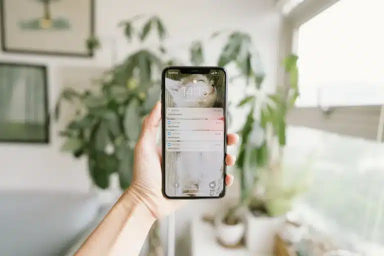 Manos anónimas sosteniendo un teléfono inteligente con notificaciones de alerta y símbolos de advertencia en la pantalla