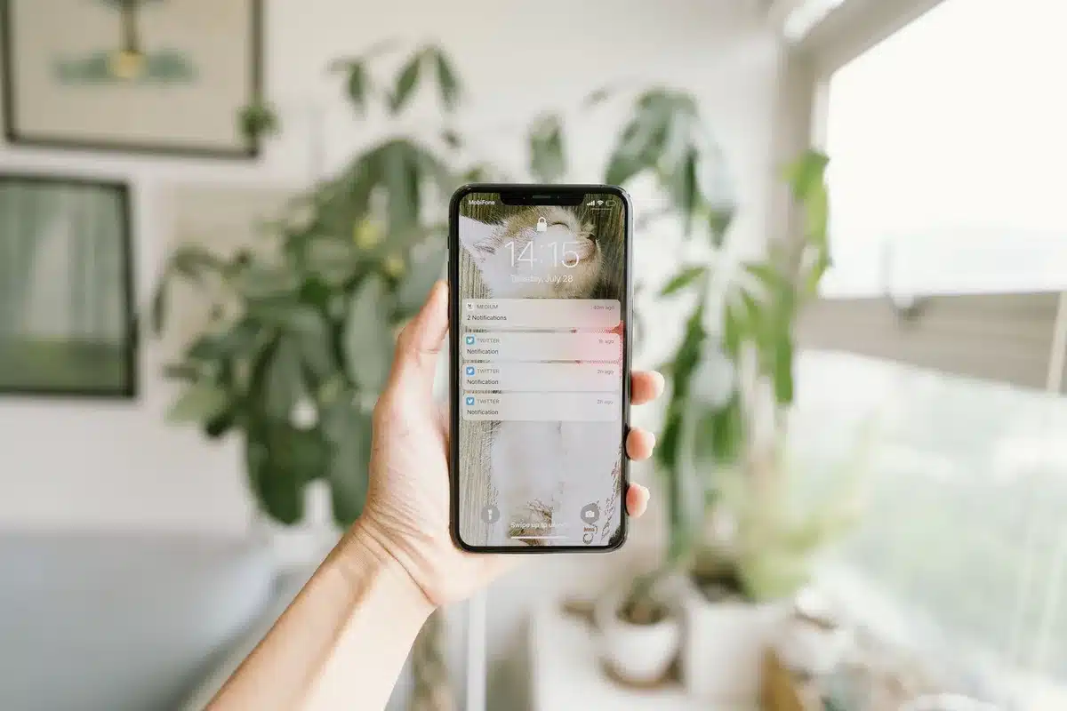 Manos anónimas sosteniendo un teléfono inteligente con notificaciones de alerta y símbolos de advertencia en la pantalla