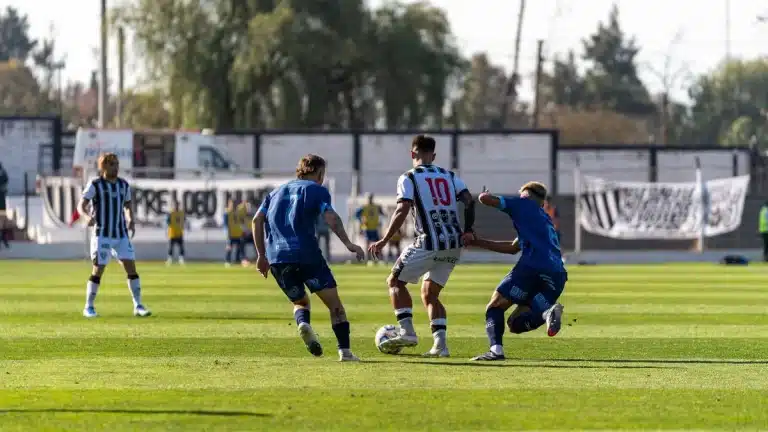 Jugadores de fútbol compitiendo intensamente por el balón durante un partido en estadio