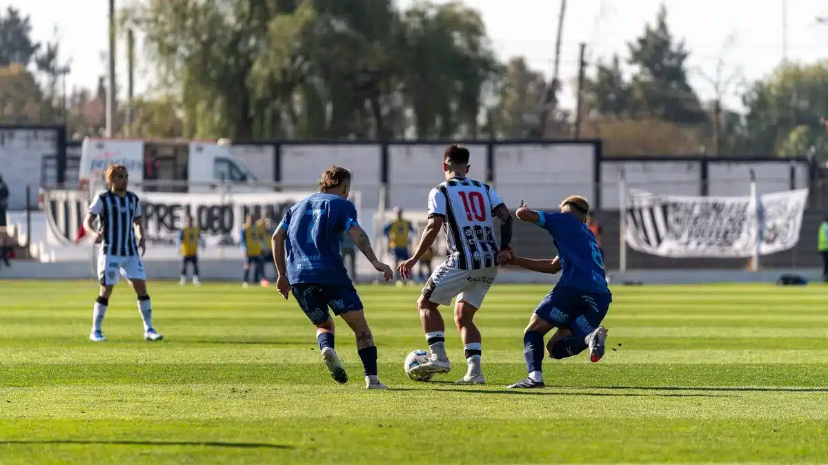 Jugadores de fútbol compitiendo intensamente por el balón durante un partido en estadio