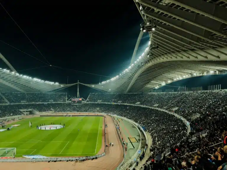 Estadio de fútbol iluminado durante un partido nocturno con multitud de aficionados